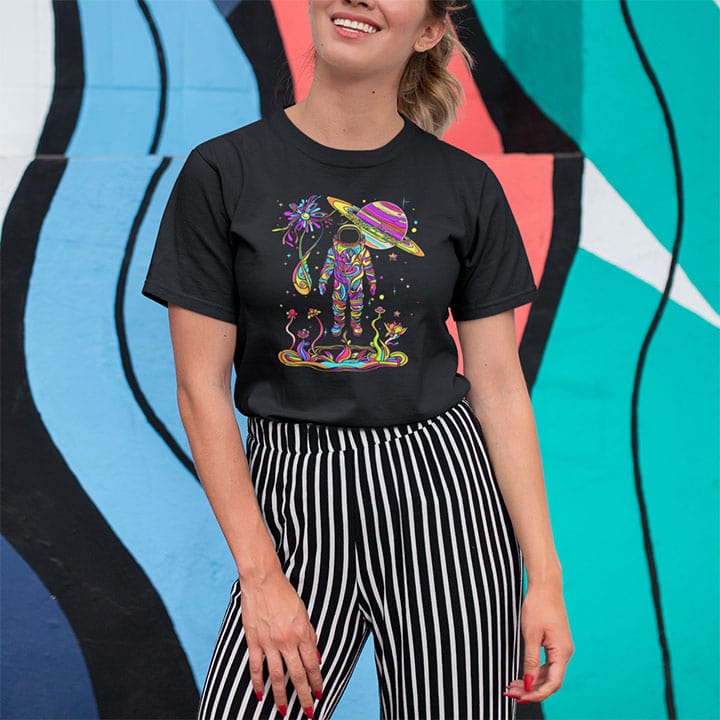 Woman wearing astronaut in vibrant rainbow garden with Saturn planet above on black t-shirt for cosmic nature mysticism.