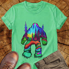 Bigfoot silhouette filled with aurora borealis and forest landscape on green t-shirt for cryptid mystery wilderness.